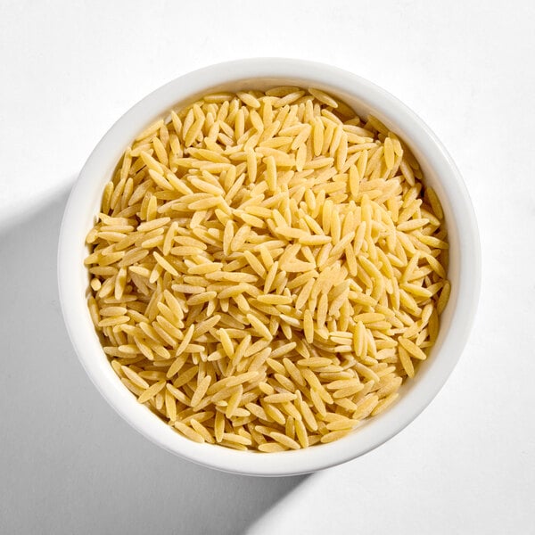 A white bowl filled with uncooked Barilla Orzo pasta.