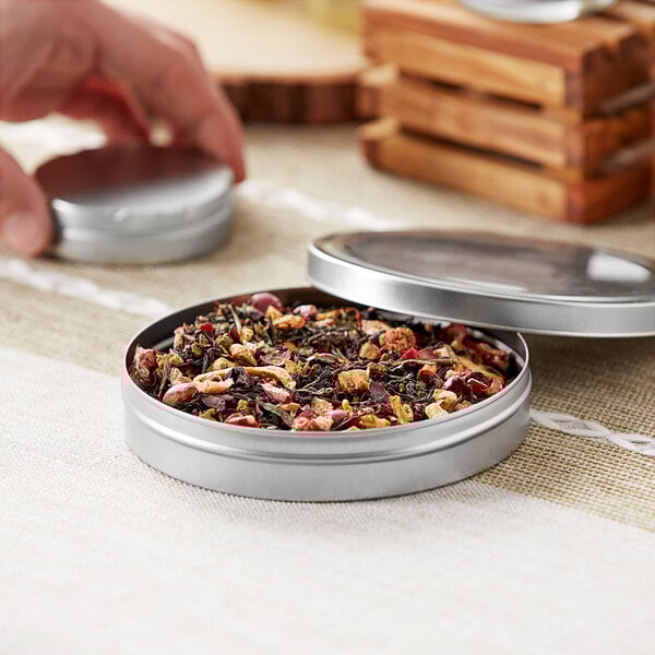 A hand holding a silver round metal tin with the lid open.