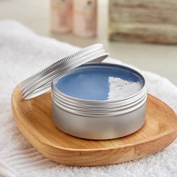 A silver tin with a ribbed top filled with blue liquid on a wooden tray.