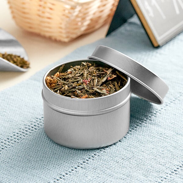 A silver deep tin with a slip cover filled with green tea leaves.