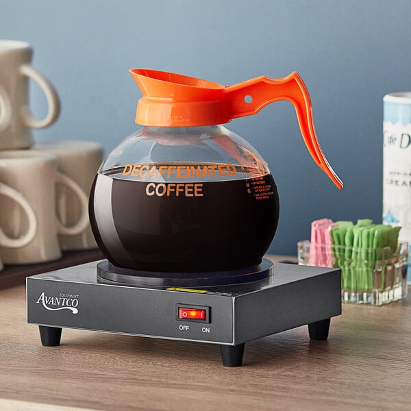 A Curtis Crystalline decaf coffee decanter with an orange handle and decaf logo on a counter.