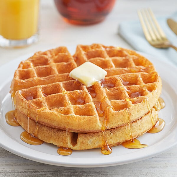 A plate with two stacked Belgian waffles topped with a pat of butter and drizzled with syrup.