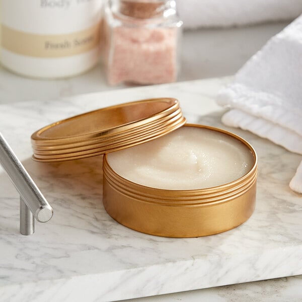 A gold flat tin with a screw top filled with a white product next to a white towel.