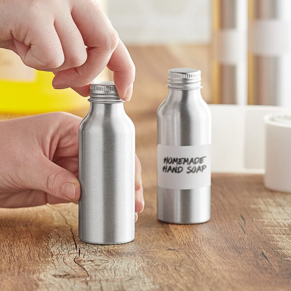 A hand labeling a silver aluminum bottle.