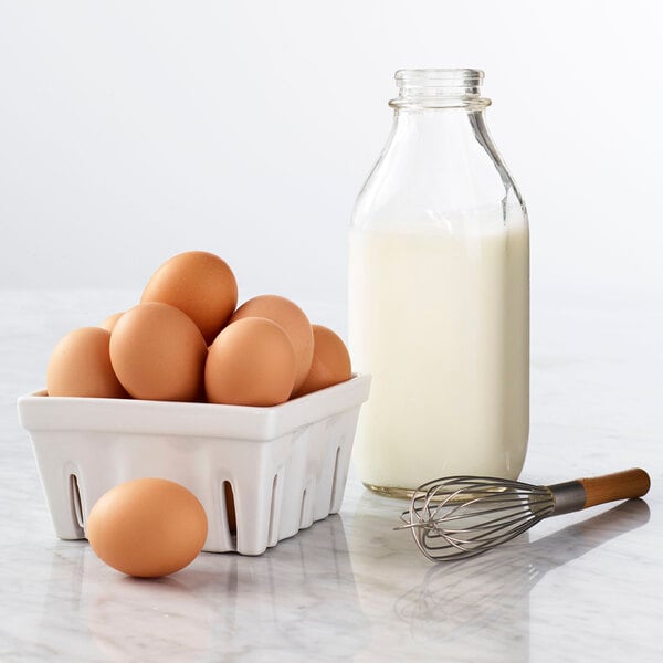 A white container of brown eggs with a whisk and a bottle of milk.