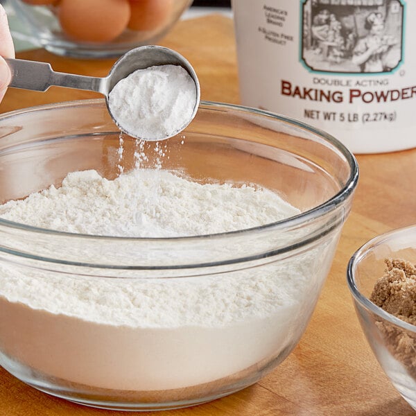 A person pouring Clabber Girl baking powder into a bowl of flour.