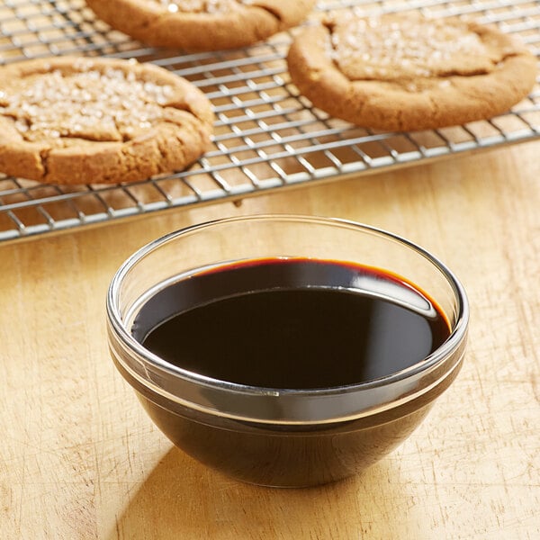 bowl of molasses in front of a cookie sheet with fresh baked molasses cookies on it