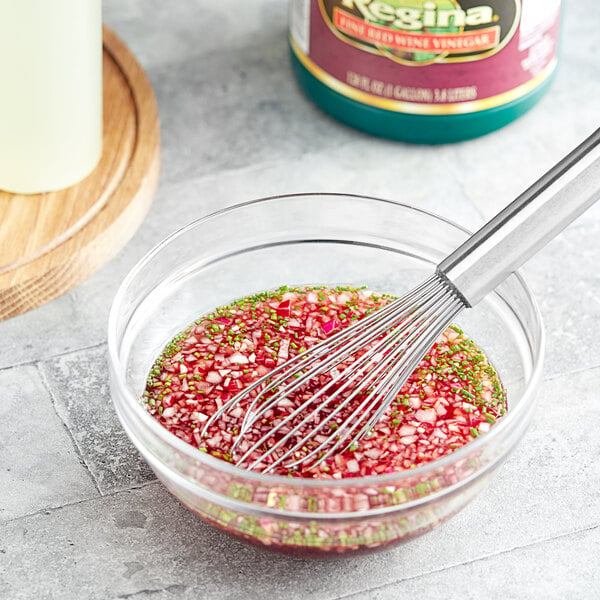 A glass bowl of red and green liquid with a whisk.