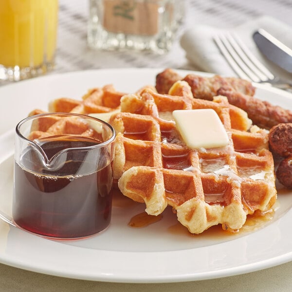 maple syrup next to waffles with butter and breakfast sausage