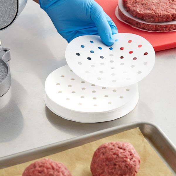 A person in blue gloves using Garde round perforated patty paper to prepare a hamburger.