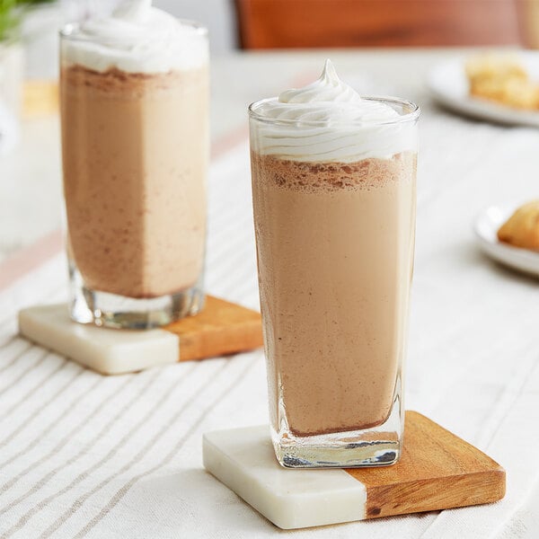 A close up of two glasses of Big Train Vanilla Chai Tea Latte with whipped cream on top.