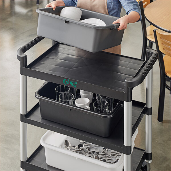 A woman holding a gray Vigor bus tub with white dishes in it.