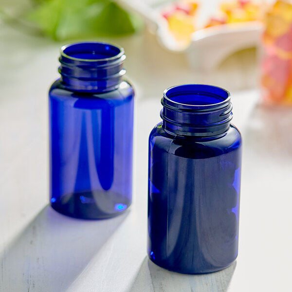 Two blue 120cc PET packer bottles with lids on a table.