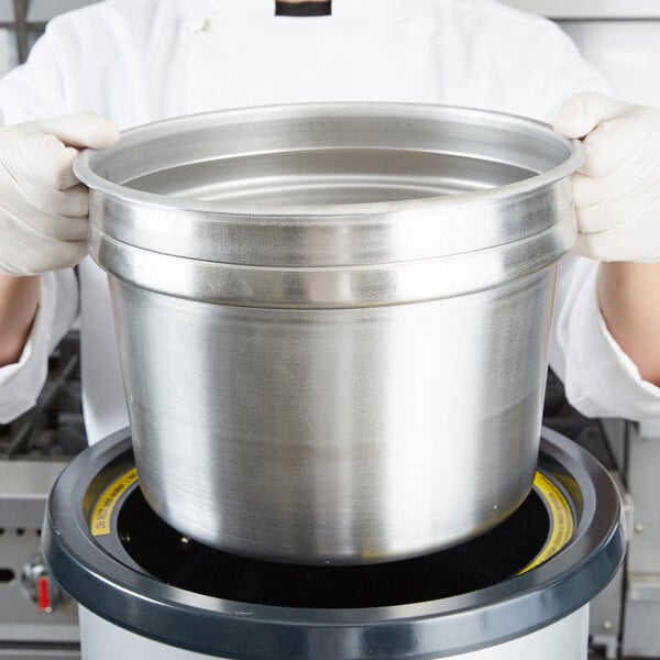 A chef holding a large silver pot.