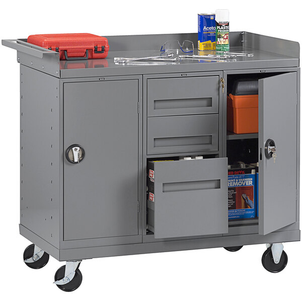 A grey Tennsco steel workbench with two drawers and a cabinet and tools on top.