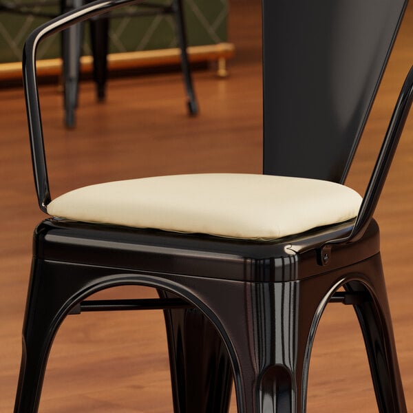 A black Lancaster Table & Seating Alloy chair with a white cushion.