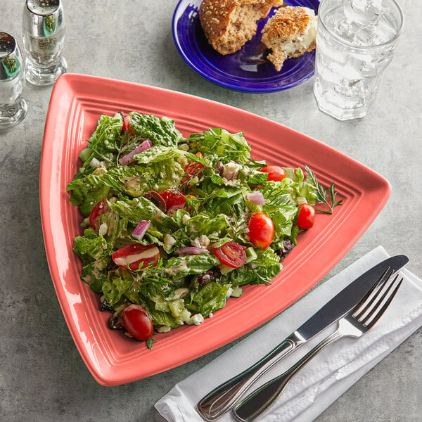 A Tuxton Concentrix Cinnebar triangle plate with a salad, fork, and knife.