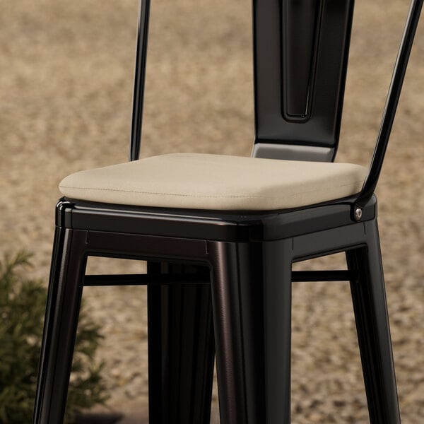 A black metal Lancaster Table & Seating chair with a tan cushion.