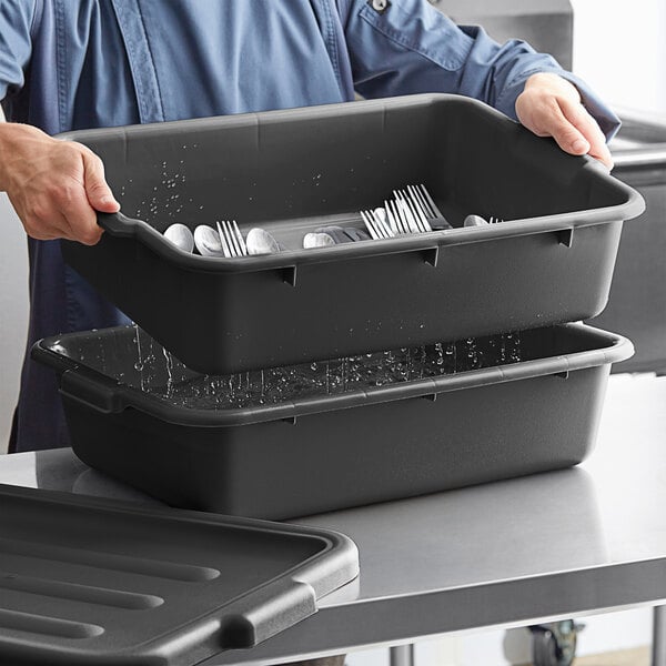 A man holding a black Choice polypropylene container with silverware in water.