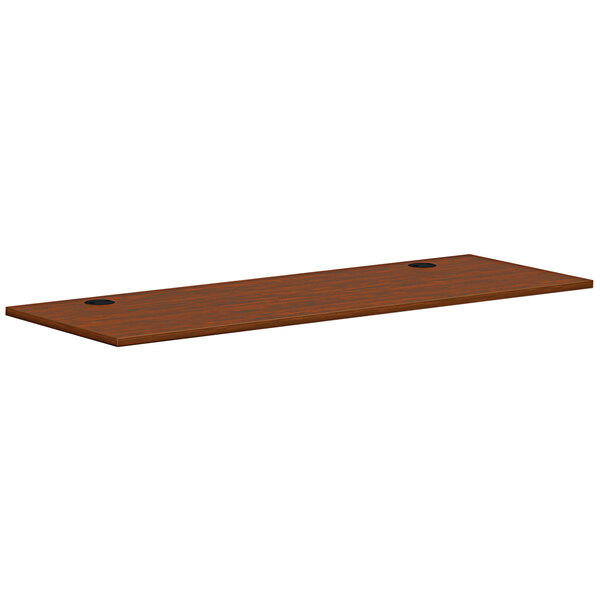 A brown rectangular wooden HON worksurface with two holes.