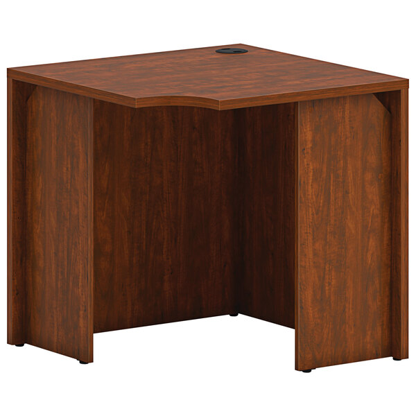 A HON russet cherry laminate corner desk shell with a hole in the top for cables.