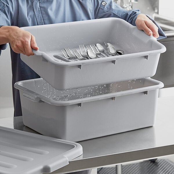 A man holding a grey Choice polypropylene drain box full of silverware.