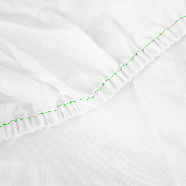 A white Monarch Brands fitted sheet with green stitching.