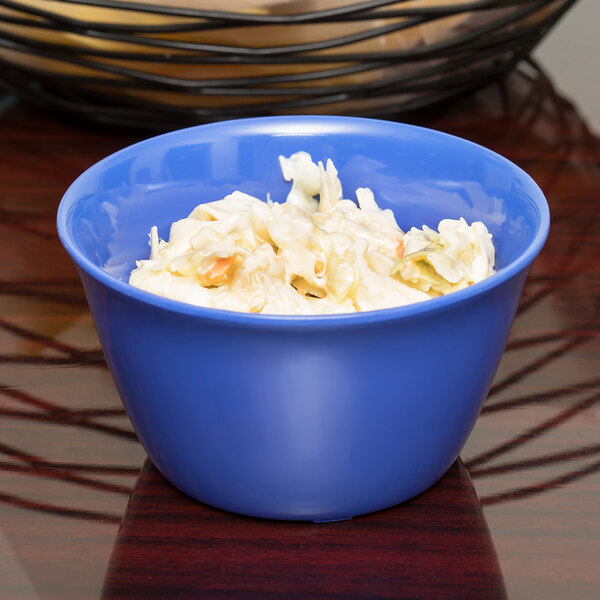 A stack of ocean blue Carlisle bouillon cups filled with coleslaw on a table.