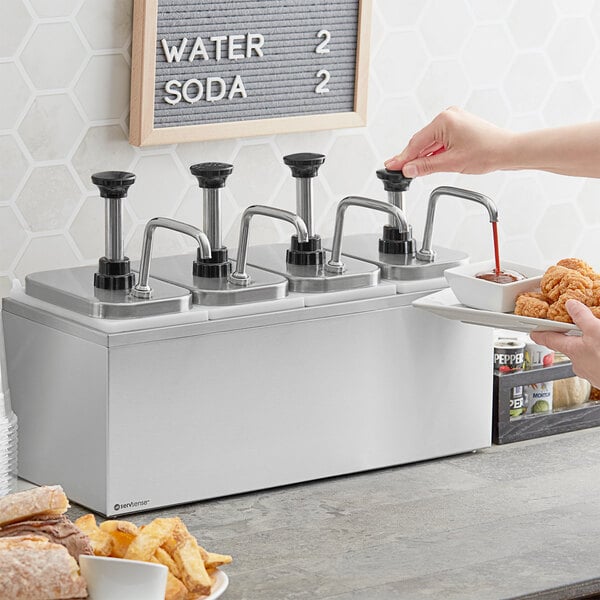 A woman using a ServSense stainless steel condiment dispenser to pour sauce onto a plate of food.