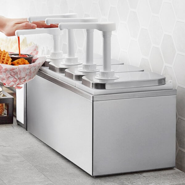 A person using a ServSense stainless steel condiment dispenser with four plastic pumps to pour sauce over fries.