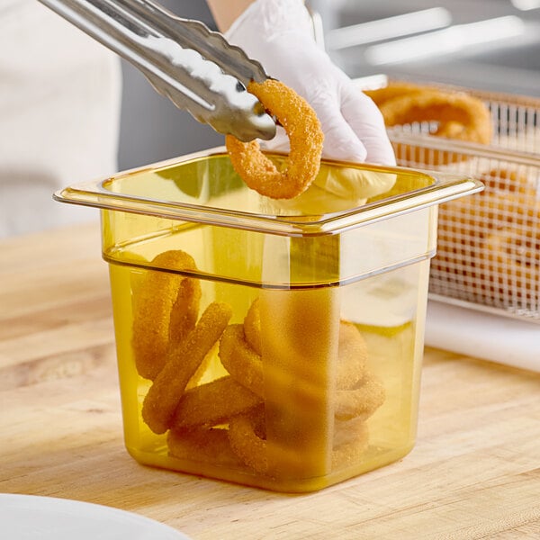 A person using tongs to serve fried onion rings from a Cambro amber food pan.