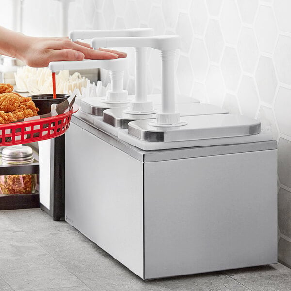A woman using a ServSense stainless steel condiment dispenser to pump condiments over a basket of fried chicken.