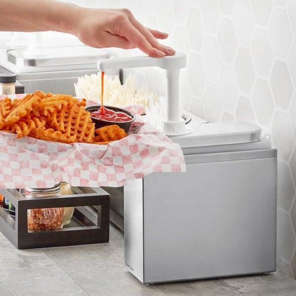 A close-up of a hand using a ServSense stainless steel pump to pour ketchup over a bowl of fries.