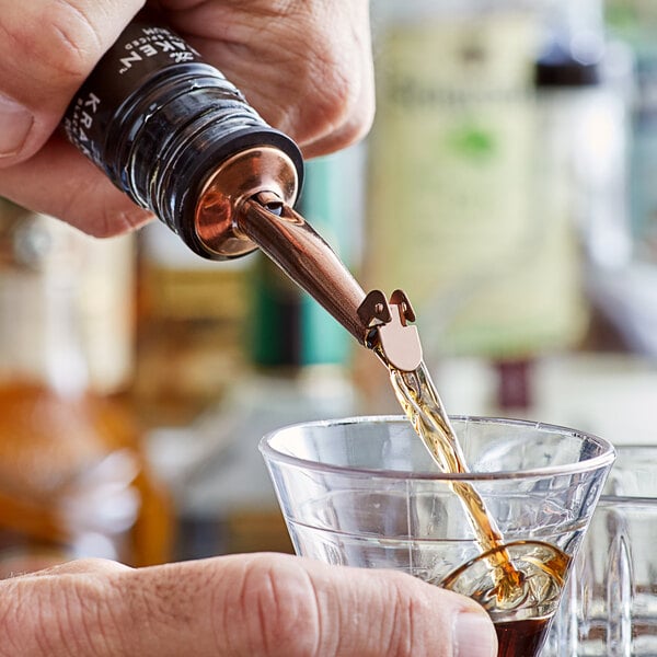 A hand using an Acopa copper liquor pourer to pour brown liquid into a glass.