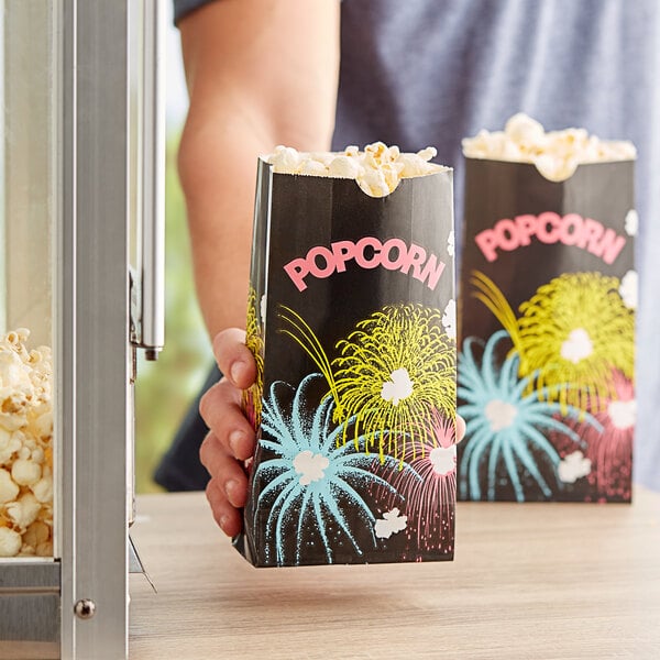 A hand holding a black Bagcraft Packaging Funburst Design popcorn bag.