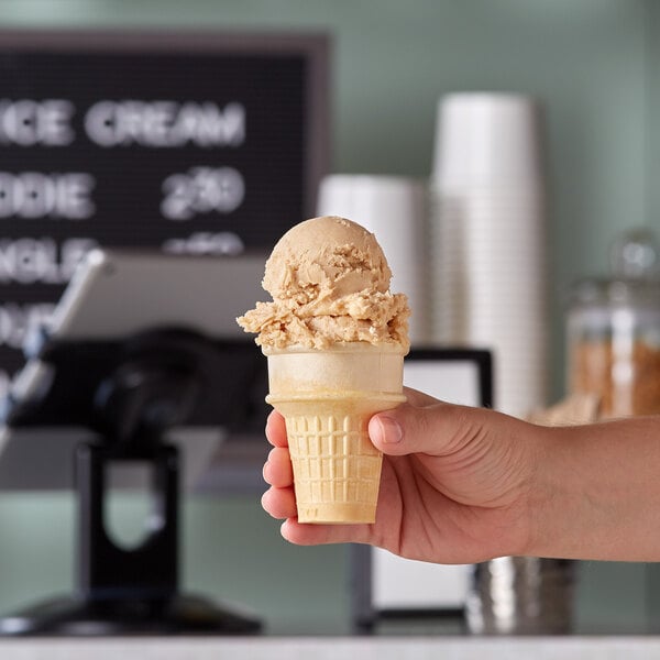 A hand holding a JOY flat bottom cake cone filled with ice cream.