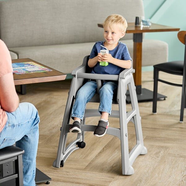 A gray Rubbermaid restaurant high chair with wheels, shown in use by a child at a dining table.