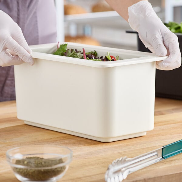 A person in white gloves using tongs to serve salad from a white Cambro food container.