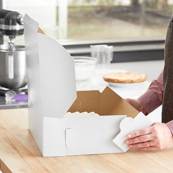 A person opening a white bakery box on a wooden table.