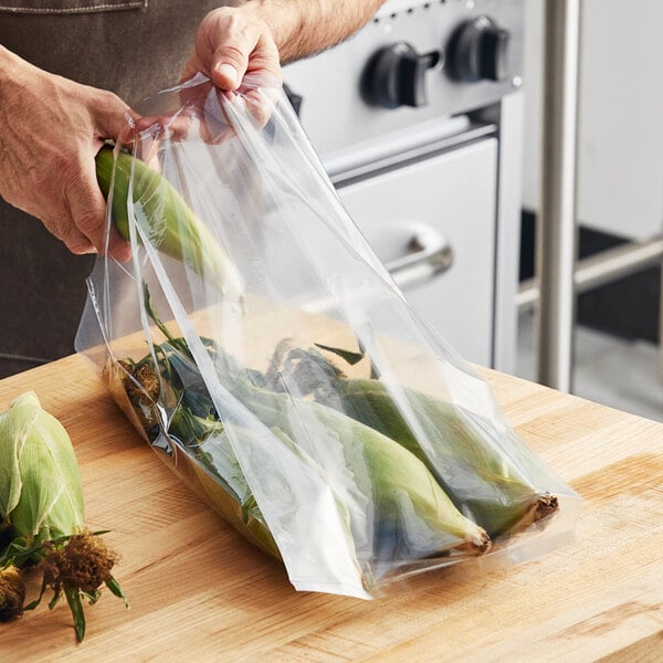 A hand holding a Choice heavy-duty plastic bag filled with corn on the cob.