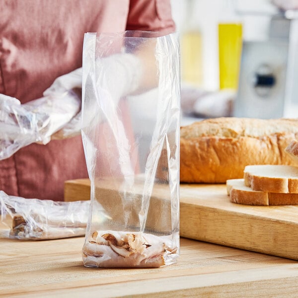 A person wearing gloves holding a Choice medium-duty plastic food bag containing meat.