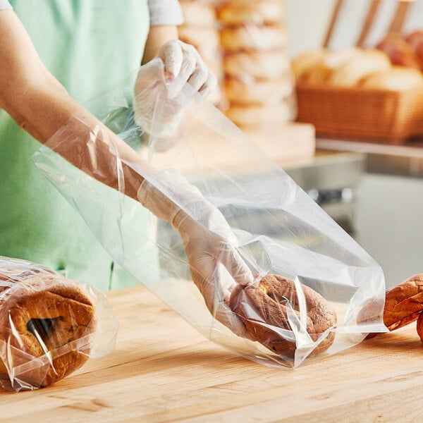 A woman wearing gloves holding a Choice medium-duty plastic food bag filled with bagels.