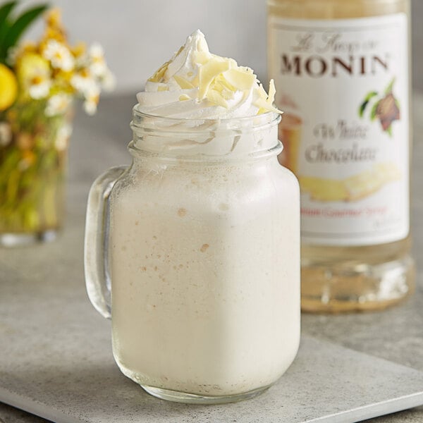 A glass mug filled with white Monin white chocolate syrup and whipped cream.