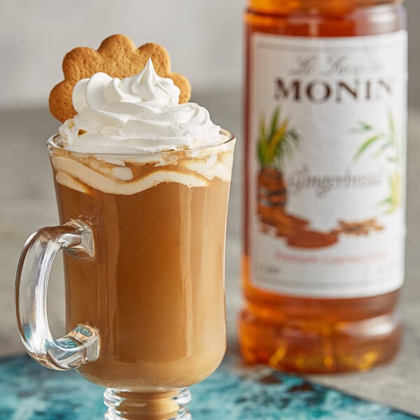 A glass mug of brown liquid with a cookie on top next to a bottle of Monin Premium Gingerbread Flavoring Syrup.