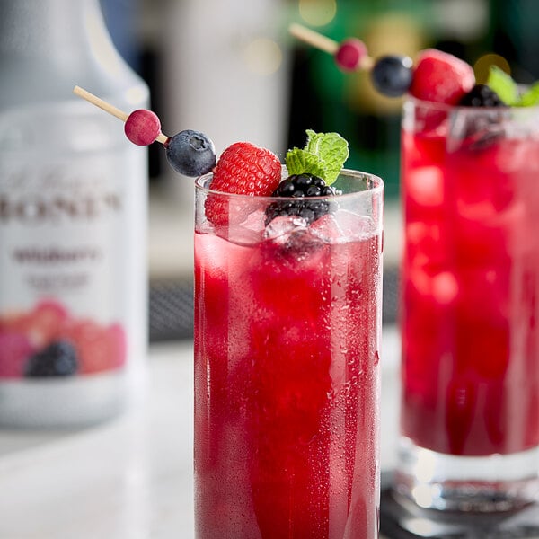 A close-up of two glasses of red wildberry drinks garnished with mint.