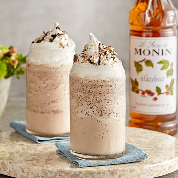 Two glasses of chocolate milkshakes with whipped cream and Monin Hazelnut syrup.