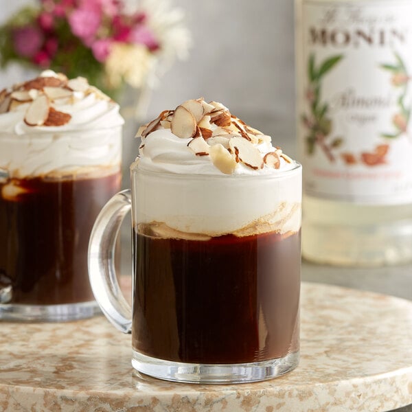 A glass mug of Monin almond flavoring syrup in coffee with whipped cream.