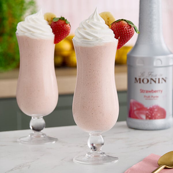 Two glasses of pink milkshakes made with Monin strawberry puree, with strawberries and whipped cream on top.