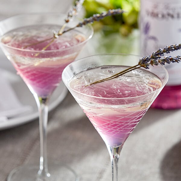 Two martini glasses of pink liquid with lavender flowers on a table in a cocktail bar.