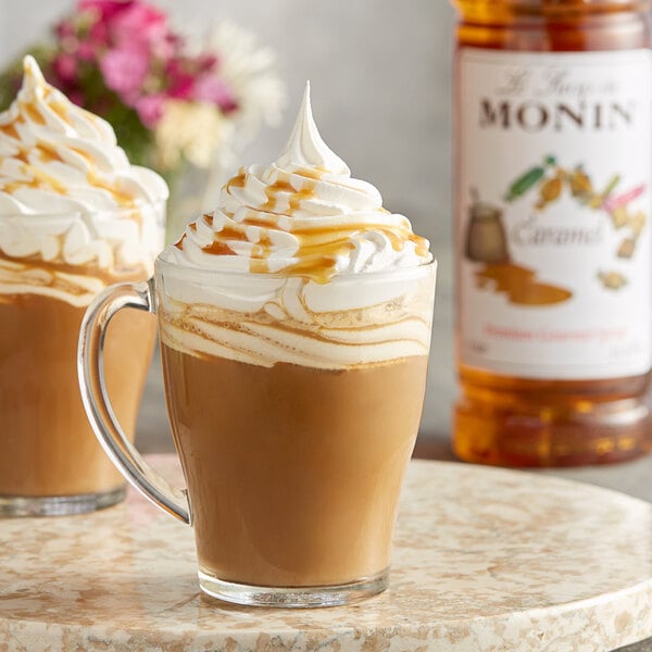 A glass mug of coffee with Monin caramel syrup and whipped cream on a marble surface.
